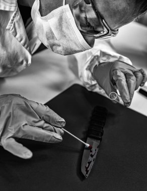 Laboratuvarda Adli Tıp. Polis uzmanı olay yeri kanıtlarını inceliyor. Bıçakta kan izleri var.