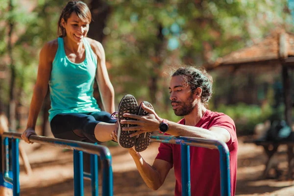 Parktaki paralel barda antrenörle egzersiz yapan bir kadın.