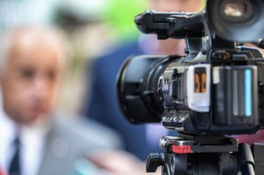 Dışarıdaki bir basın toplantısında çalışan kamera operatörü. Gazeteciler bir medya etkinliğinde resmi giyinmiş siyasetçi veya işadamıyla röportaj yapıyorlar. 