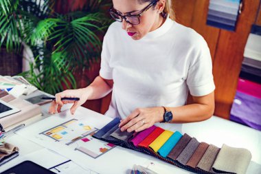 Ofisindeki kumaş örneklerine bakan kadın dekoratör.
