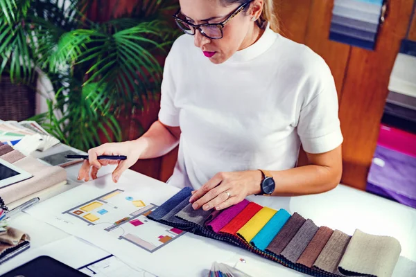Ofisindeki kumaş örneklerine bakan kadın dekoratör.