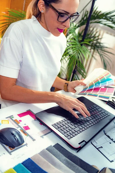 Mimar, iç mimar, malzeme örnekleri ve ofiste dizüstü bilgisayar üzerinde çalışıyor.