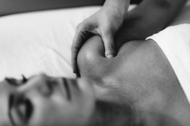 Fizyoterapist, omzu yaralı kadın hastaya masaj yapıyor. Spor sakatlığı tedavisi.