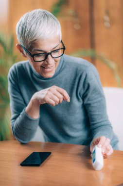 Temas Olmayan Dijital Termometreyle Kıdemli Kadın Vücut Sıcaklığını Kaydediyor, Akıllı Telefon Uygulaması Kullanılıyor
