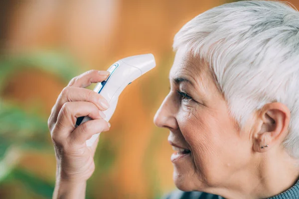 Senior Woman Measuring Body Temperature with Contactless Digital Thermometer at Home