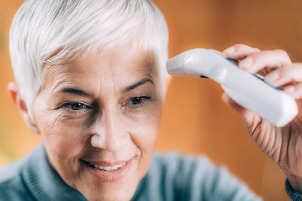 Улыбающаяся Пожилая Женщина Измеряет Температуру Тела Бесконтактным Цифровым Термометром — стоковое фото