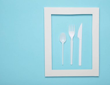 Plastik çatal bıçak takımı mavi bir arka plan üzerinde beyaz bir çerçeve içinde piknik için. Bir tek kullanımlık kaşık, çatal, bıçak. Üstten görünüm, minimalist eğilim