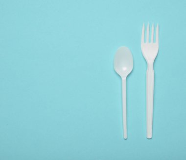 Beyaz plastik çatal bıçak takımı mavi bir arka plan üzerinde piknik için. Tek kullanımlık kaşık, çatal. Üstten görünüm, kopya alanı