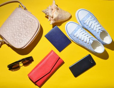 Kadın trendy seyahat aksesuarları ve teknoloji gadget'lar sarı yüzeyde. Spor ayakkabı, pasaport, çanta, Gözlük, smartphone, güç banka, kabuk. Üstten görünüm. Düz yatıyordu.