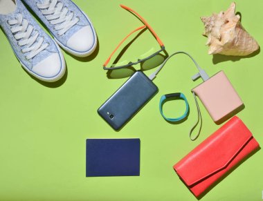 Kadın trendy seyahat aksesuarları ve teknoloji gadget'lar yeşil yüzey üzerinde. Spor ayakkabı, pasaport, çanta, Gözlük, smartphone, güç banka, kabuk, akıllı bilezik. Üstten görünüm. Düz yatıyordu.