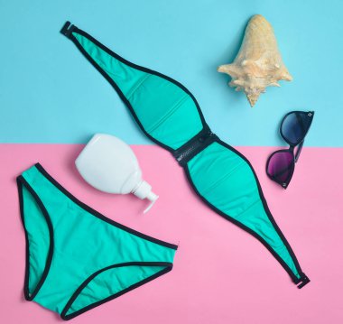 Pastel renkli bir arka plan üzerinde sahilde tatil için aksesuarlar. Mayo, Güneş kremi, güneş gözlüğü, kabuk. Üstten görünüm.