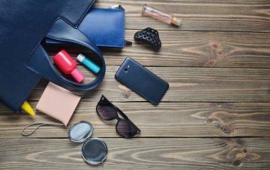Kadınların çantada ne var? Ahşap arka plan üzerinde kadın moda aksesuarları. Smartphone, parfüm şişesi, güç banka, ayna, güneş gözlüğü, ruj. Üstten görünüm.