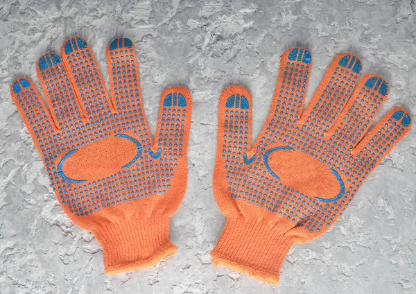 Orange work gloves on a gray concrete background. Top view