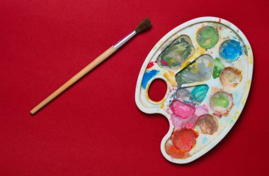 Plastik palet guaj boya ve fırça kırmızı Kağıt arka plan ile. Üstten görünüm
