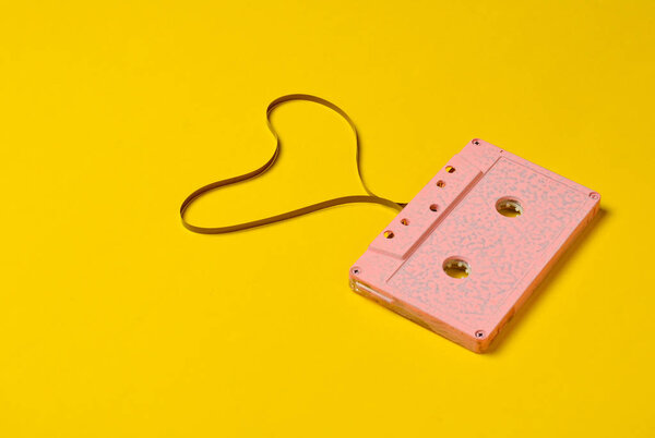Heart shape from audio cassette tape over yellow paper background, top view. Hipster Love