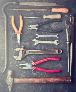 Siyah bir beton tablo üzerinde birçok çalışma araçları. Kerpetenler, dosya, pense, hurda, çekiç, anahtar, tornavida. Üstten görünüm. Düz yatıyordu.