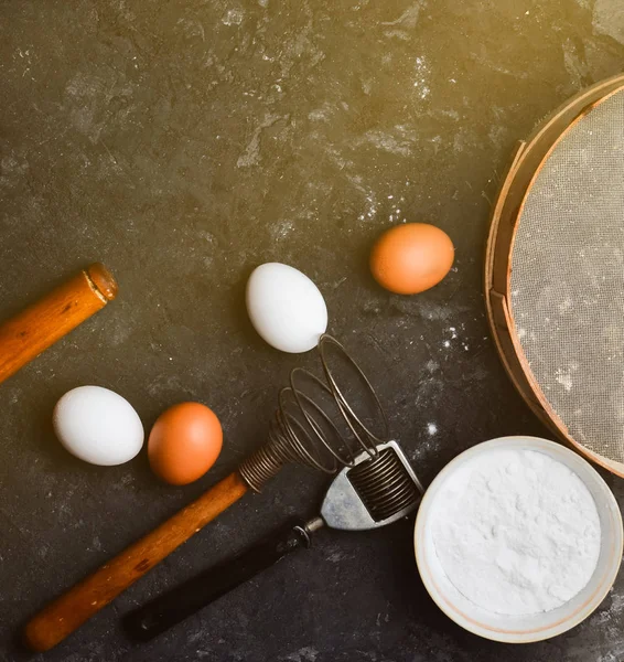 Ingredients for pasta. The cooking process. Eggs, flour, kitchen tools on a black concrete table. Tools for cooking. Italian cuisine.Top view. Flat lay.