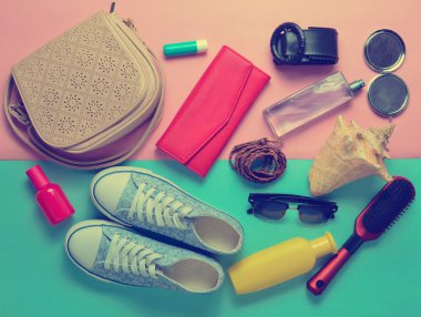 Girly şık bahar ve yaz aksesuarları: spor ayakkabı, kozmetik, güzellik ve hijyen ürünleri, bir çanta, pastel pembe mavi arka plan üzerinde güneş gözlüğü. Kadınların çantada ne var? Bir seyahate.