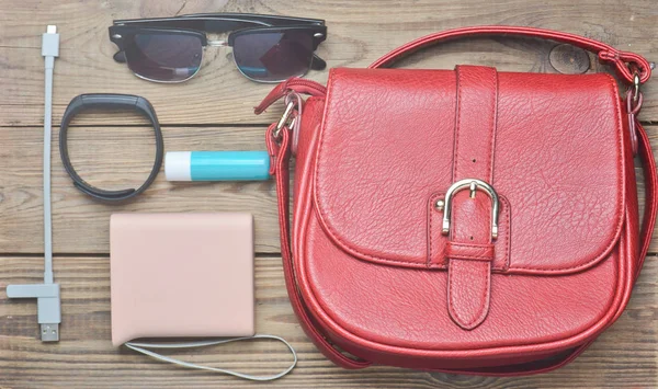 Red leather bag and other female accessories layout on a wooden desk. Top view. Trend of minimalism. Flat lay.