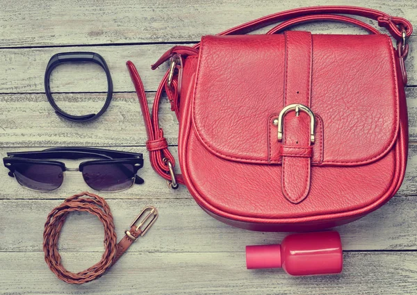 Red leather bag and other female accessories layout on a wooden desk. Top view. Trend of minimalism. Flat lay.