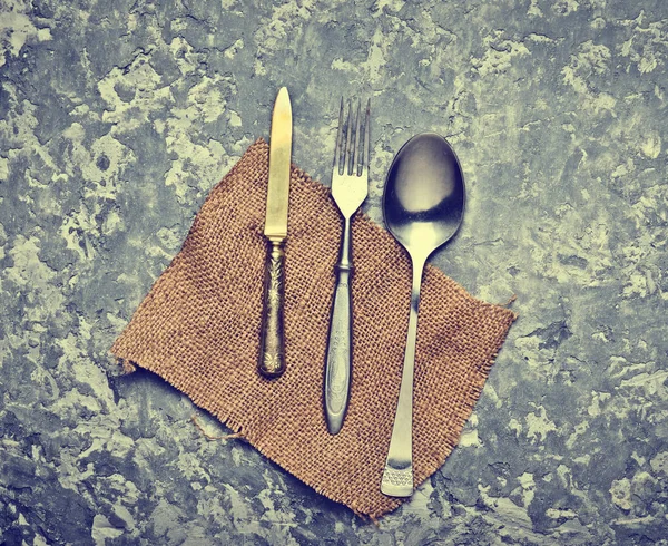 Antique spoon, fork, knife on a napkin lie on a gray concrete table. Top view.