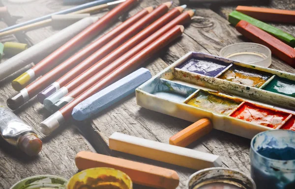 A group of products for drawing and creativity on a wooden table. Rustic style. Gouache, oil painting, watercolor paints, crayons, pencils.
