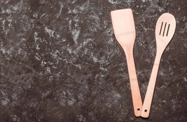 A wooden spatula and a spoon for cooking on a black concrete table. Space for text. Top view.