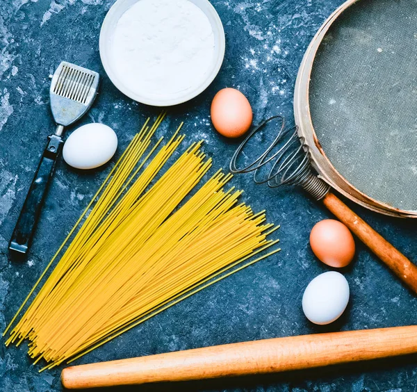 Ingredients for pasta. The cooking process. Eggs, flour, kitchen tools on a black concrete table. Tools for cooking. Italian cuisine.Top view. Flat lay.