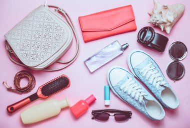 Kadınların çantada ne var? Bir geziye gidiyor. Girly şık bahar ve yaz aksesuarları: spor ayakkabı, kozmetik, güzellik ve hijyen ürünleri, bir çanta, pastel pembe bir arka plan üzerinde güneş gözlüğü. Üstten Görünüm.