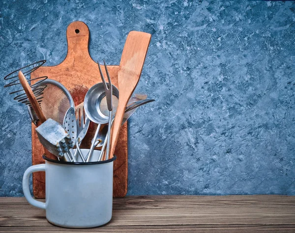 Kitchen tools for cooking on a wooden table on the background of a concrete wall.Copy space. Spoons, forks, wooden spatula.