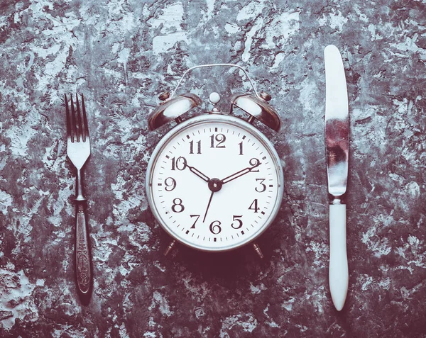 Time for breakfast. Alarm clock, fork and knife on a concrete table. Top view. Flat lay.