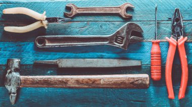 Mavi ahşap arka plan üzerinde bir çalışma aracı: tornavida, pense, hurda, çekiç, kerpeten, dosya, ayarlanabilir anahtarı. Üstten Görünüm.