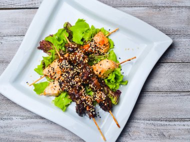 Yakitori bir plaka üzerinde susam ile. Kızarmış tavuk et ve tavuk karaciğer ahşap bir masa üzerinde sopa üzerinde.