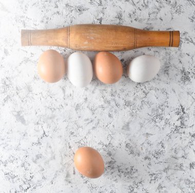 Yumurta, oklava beyaz beton yüzeyi. Pişirme işlemi, malzemeler ve çatal bıçak takımı mutfak aletleri.