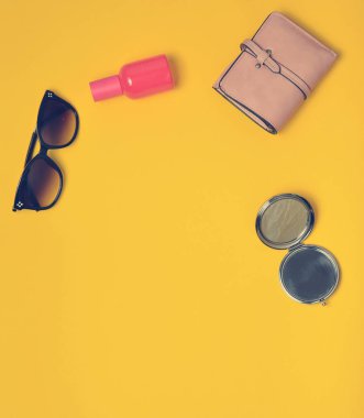 Sarı bir arka plan üzerinde izole kadın aksesuarları. Güzellik ve moda için ürünler. Güneş gözlüğü, bir çanta, parfüm şişe, bir ayna. Üstten Görünüm. Uzay kopyalayın. Düz yatıyordu.