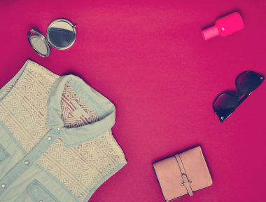 Kadın aksesuarları ve giyim kırmızı bir arka plan üzerinde. Kot gömlek, ayna, parfüm şişesi, güneş gözlüğü, çanta. Uzay kopyalayın. Düz yatıyordu. Üstten Görünüm.