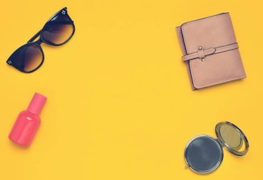 Sarı bir arka plan üzerinde izole kadın aksesuarları. Güzellik ve moda için ürünler. Güneş gözlüğü, bir çanta, parfüm şişe, bir ayna. Üstten Görünüm. Uzay kopyalayın. Düz yatıyordu.