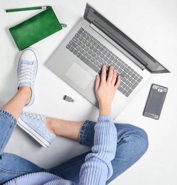 Modern bir genç kız bir beyaz zemin ve kullanımı bir dizüstü bilgisayar üzerinde oturur. Nesil z. Freelancing kavramı. Çalışma alanı. Üstten Görünüm.