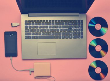 Dizüstü bilgisayar, smartphone, güç banka, Cd sürücüleri, pembe bir arka plan üstünde Usb birden parlamak götürmek. Modern ve eski dijital medya ve becerikli alet.