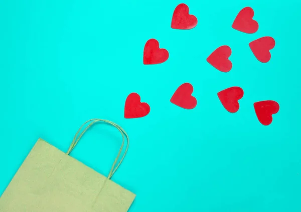 The concept of love of shopping. A paper bag for shopping and lots of decorative hearts on a yellow background. Valentine's Day. Top view.