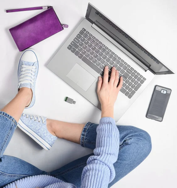 Modern bir genç kız bir beyaz zemin ve kullanımı bir dizüstü bilgisayar üzerinde oturur. Nesil z. Freelancing kavramı. Çalışma alanı. Üstten Görünüm.