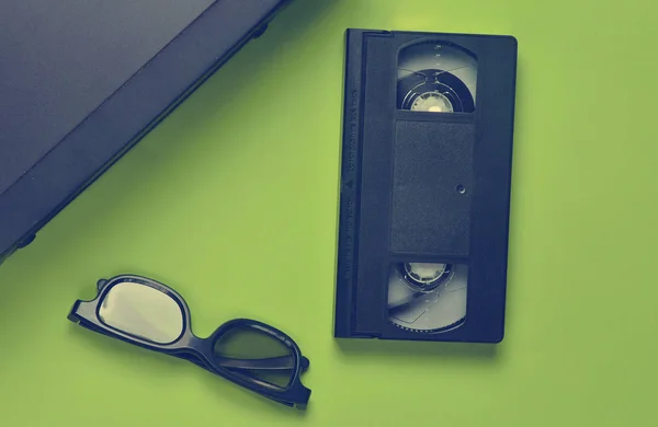 Vhs player, video cassette, 3d glasses on a green background. Obsolete media technologies. Top view.