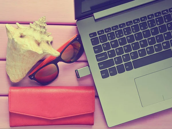 The concept of web work at a beach resort, freelancing. Laptop, flash drive, sunglasses, shell, purse on a violet color wooden table. Top view.