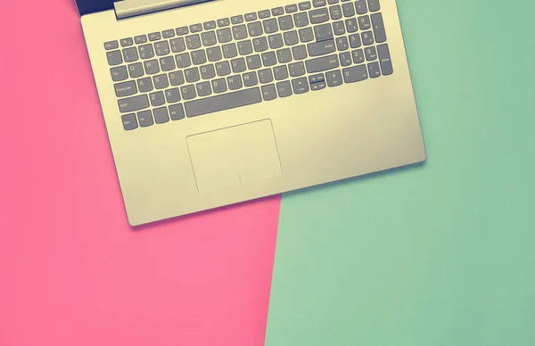 Fragment of a laptop on a colored paper background. Keyboard, touchpad. Modern digital technologies. Copy space. Top view.