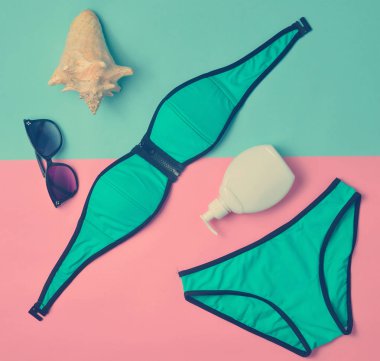 Pastel renkli bir arka plan üzerinde sahilde tatil için aksesuarlar. Mayo, Güneş kremi, güneş gözlüğü, kabuk. Üstten görünüm.