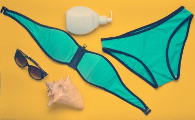 Sarı bir arka plan üzerinde sahilde tatil için aksesuarlar. Mayo, Güneş kremi, güneş gözlüğü, kabuk. Üstten görünüm.
