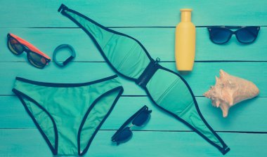 Beach resort ve mavi ahşap arka plan üzerinde Araçlar için aksesuarlar. Mayo, akıllı bilezik, Güneş kremi, güneş gözlüğü, kabuk. Üstten görünüm.