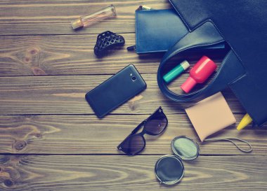 Kadınların çantada ne var? Ahşap arka plan üzerinde kadın moda aksesuarları. Smartphone, parfüm şişesi, güç banka, ayna, güneş gözlüğü, ruj. Üstten görünüm.