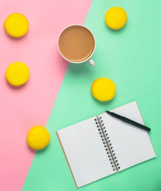 Defter bir kalem, bir fincan kahve ve sarı macaroons pastel renkli arka plan ile. Minimalizm eğilimini. Üstten görünüm. Düz yatıyordu.