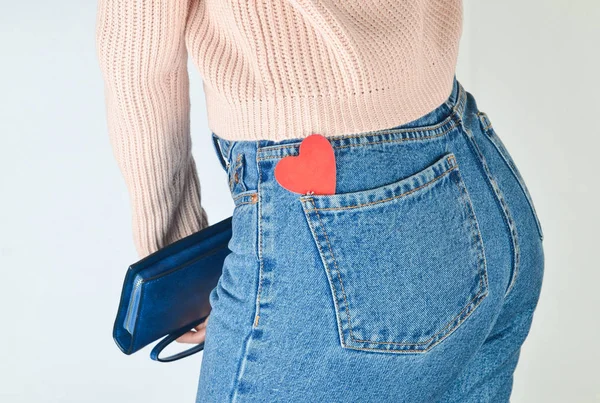 在一个苗条女孩的牛仔裤后袋的装饰心脏在她手中的钱包在白色背景 侧面视图 — 图库照片